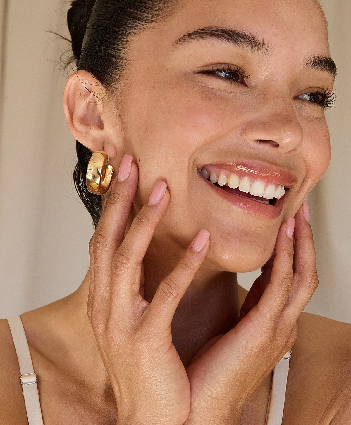 Model showcasing gold earrings and smiling brightly.
